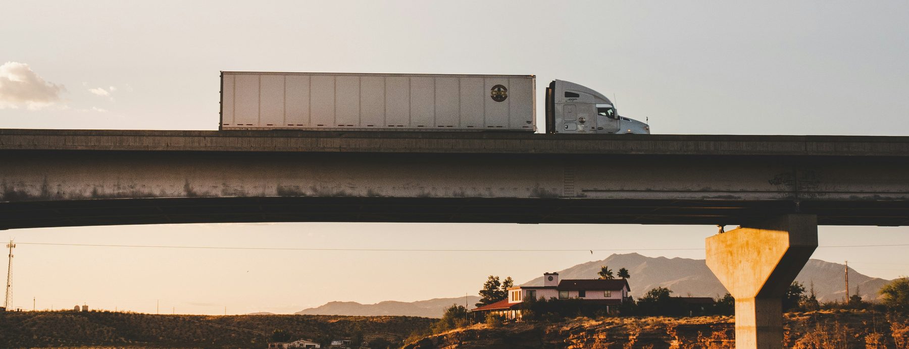 Freight truck with a white trailer crossing a highway bridge at sunset